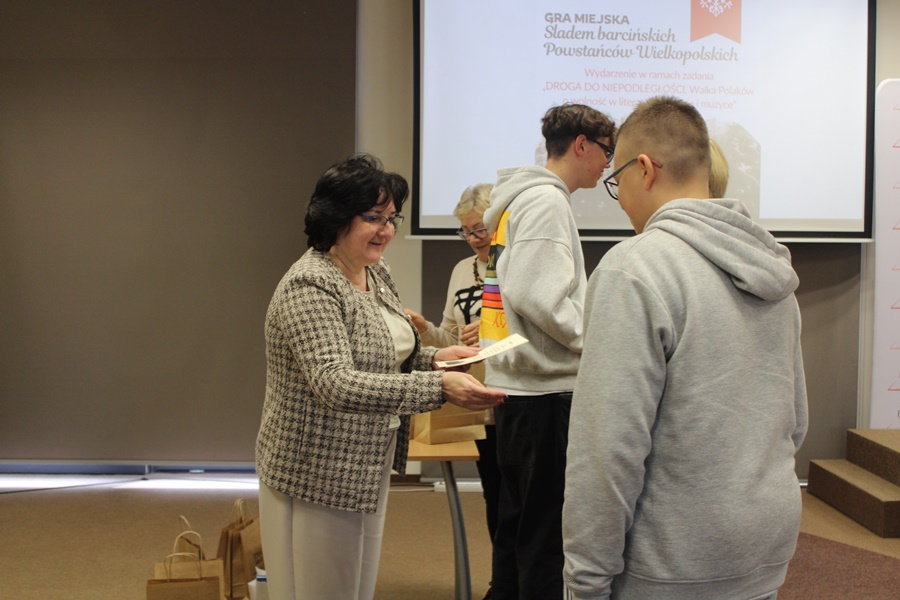 Dyrektorka biblioteki podając rękę wręcza uczestnikowi dyplom za udział w grze miejskiej