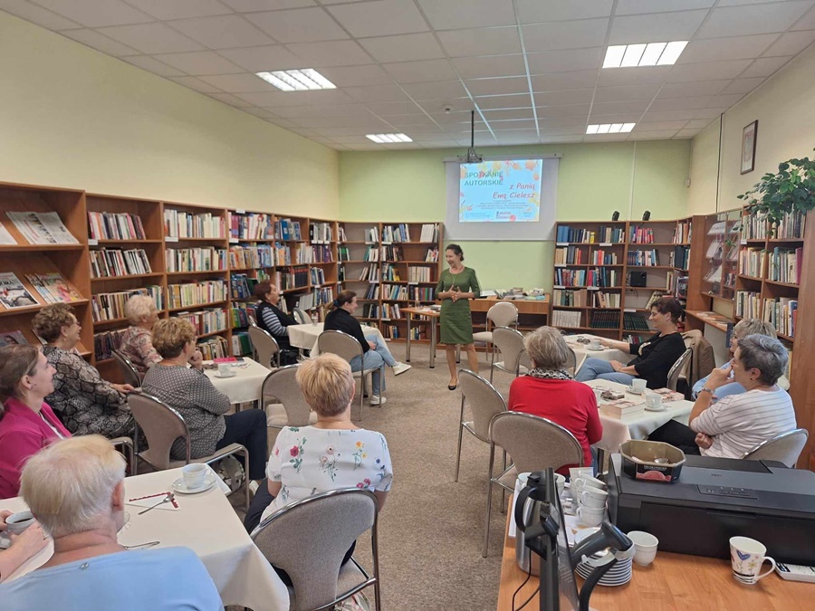 Publiczność siedzi na krzesłach, przed nimi stoi zaproszona autorka 